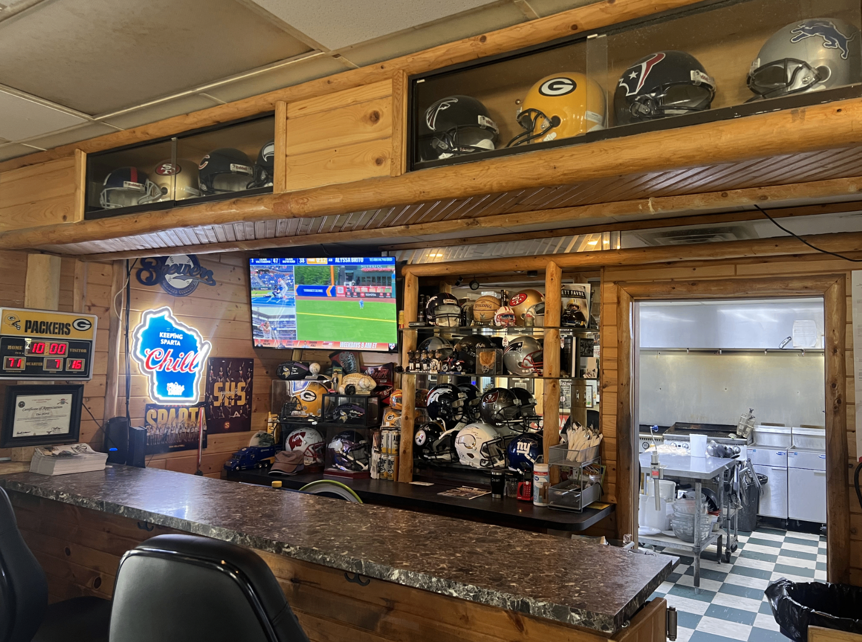 Wood-paneled bar inside The Zone with a TV showing baseball and shelves of sports helmets