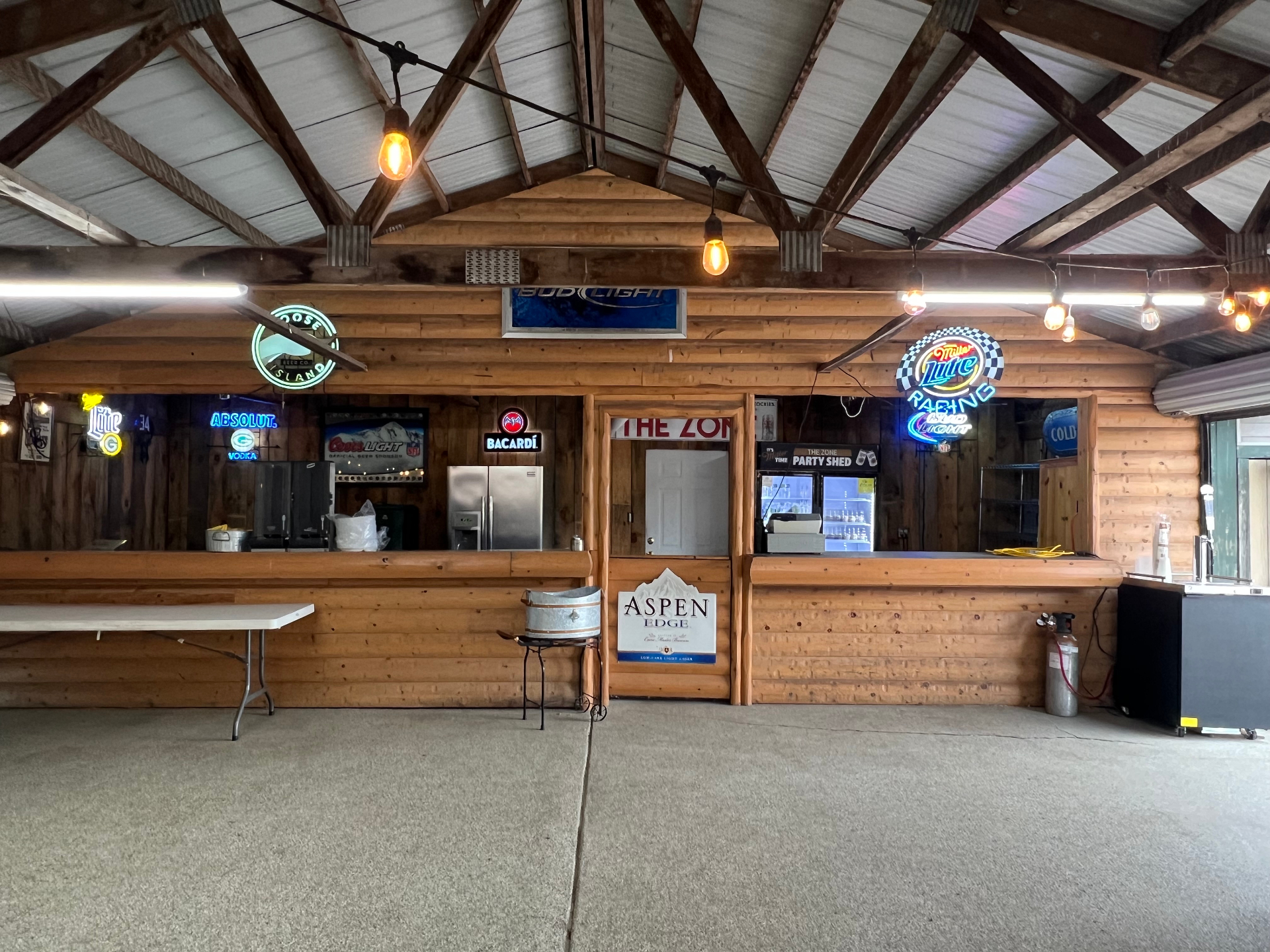 Wide interior view of The Party Shed at The Zone with open roll-up doors and rows of tables