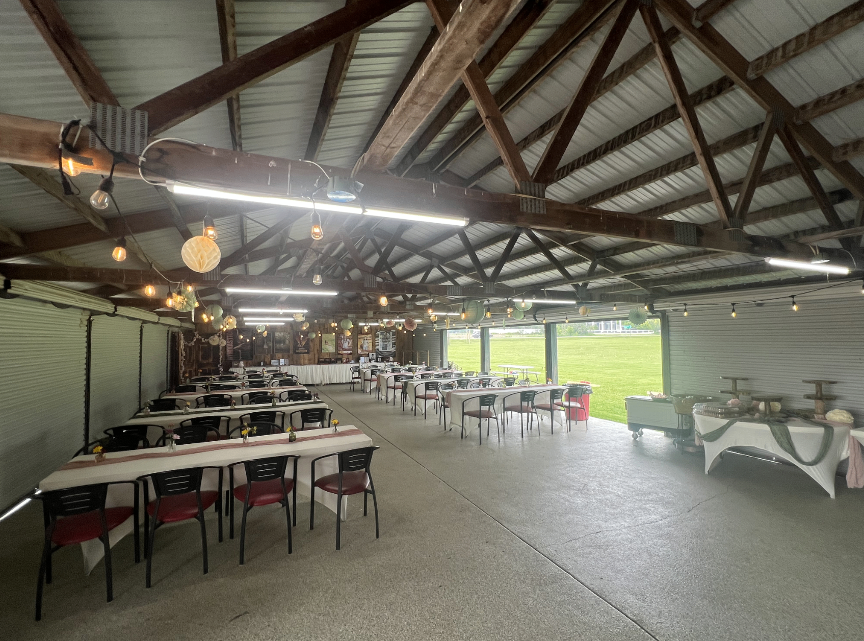 Wide view of The Party Shed with open roll-up doors overlooking the grass